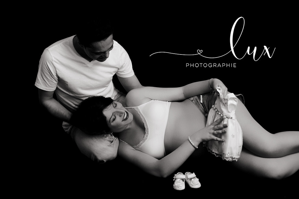 Maternity photography West-Island. Man and pregnant woman sitting on the floor and looking at baby clothing.