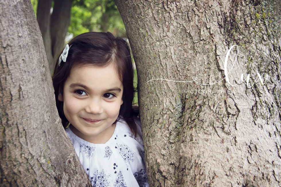 Montreal family photographer. Little girls looking through the branches of a tree.