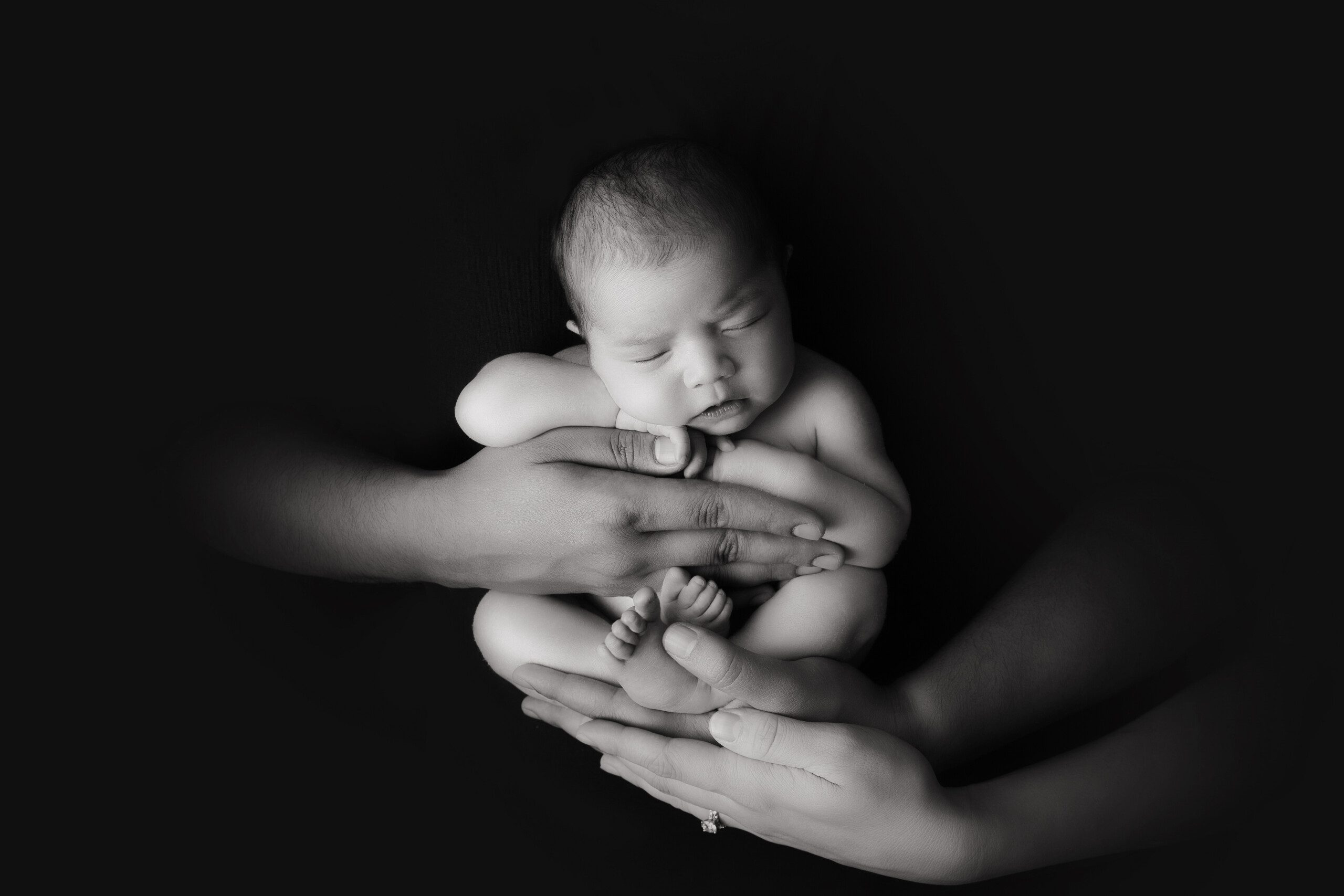 Montreal Newborn Photographer. Newborn baby being held in the arms of her mom and dad.