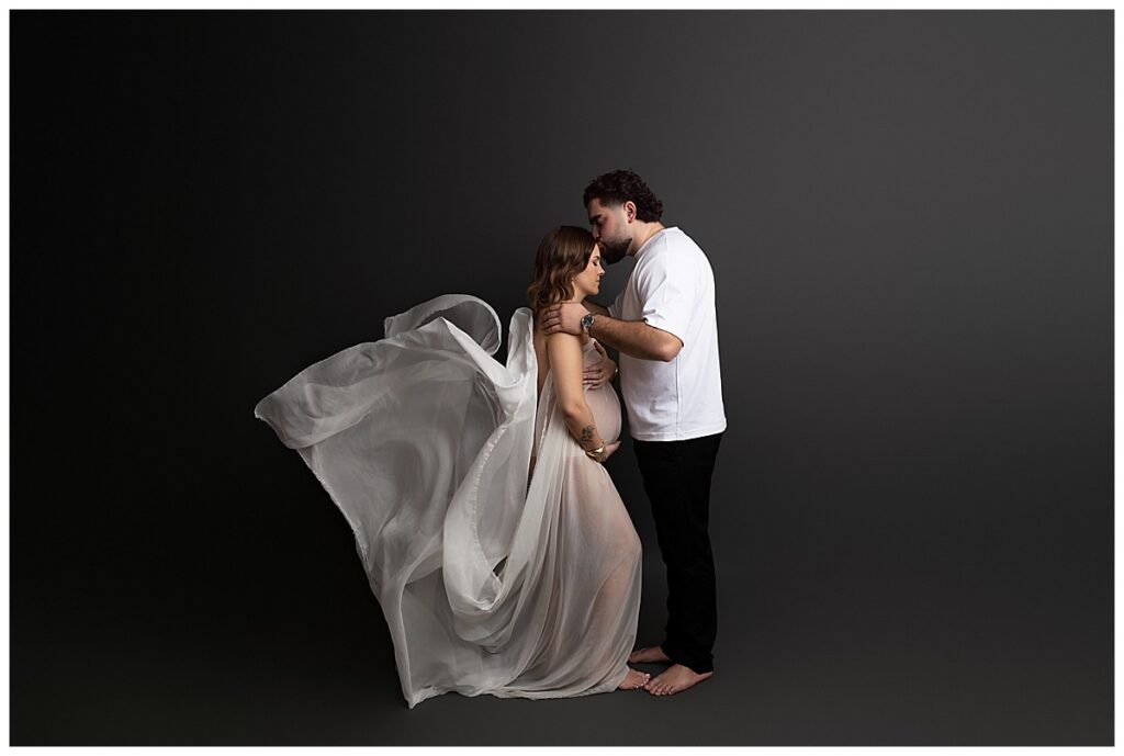 Editorial maternity photoshoot with flowing fabric and dramatic movement in studio setting